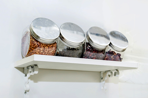 set of glass containers for spices and cereals on a white shelf on the wall