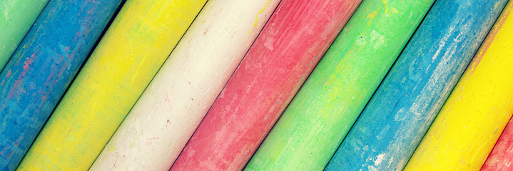 A row of multi-colored crayons lying in a dense diagonal pattern. Horizontal banner