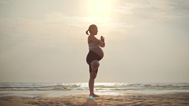 Young Pregnant woman practicing yoga at the beach