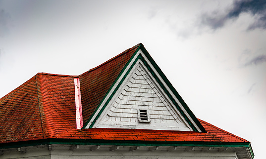 Weathered red roof with wooden trim and peeling paint on an old wooden building under a stormy sky