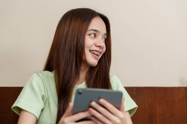 Asian Youthful learner interacts with tablet, cheerful demeanor illuminating homely workspace. Beaming student navigates through tablet, joviality complementing cozy ambiance of her study room.