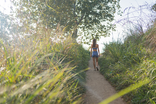 Young woman hikes up path through lush meadow