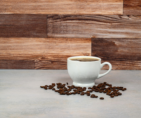 Coffee in porcelain cup with roasted coffee beans on table