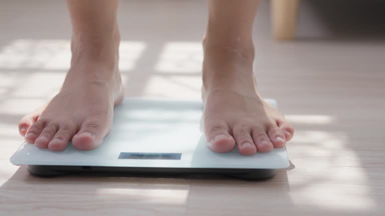 Close-up of A Woman feet stepping on digital measuring weight scales to check body weight scales with barefoot. Weighing measuring for food control. Healthy care and wellbeing concept.