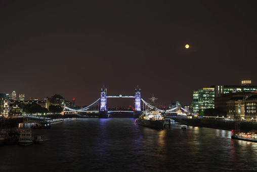 Full moon rising over the illuminated Tower Bridge, the HMS Belfast museum ship and the River Thames, London, UK
