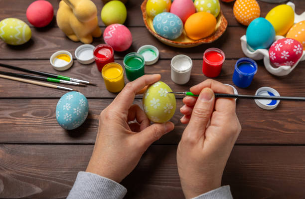 istock Woman paints Easter eggs at the kitchen wooden table.Happy Easter celebration concept.Colorful Easter eggs with different patterns.Paints,decorations for coloring eggs for holiday.Creative background. 2091593952
