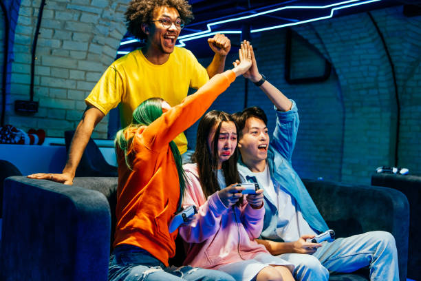 Multiethnic group of young friends playing videogames at home sitting on the sofa - Videogamers having fun playing e-sports at computer videogame console
