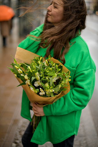 Wonderful flowers in a hands of a tenderness girl in a green jacket and black jeans on the street