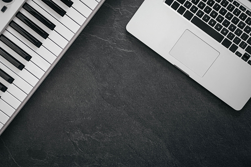 Musical keys and laptop on a textured black background, flat lay, concept of music making and musical creativity. Copy space.