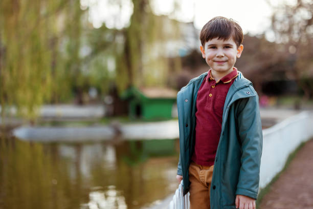 A joyful boy in a white shirt and hat dances near a fast-flowing river in a lush green forest area, surrounded by trees and natural scenery.