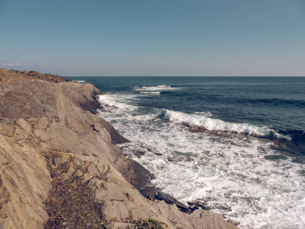 From above of foamy blue sea washing rocky coast with cliffs under cloudless blue sky