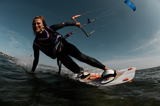 Smiling girl in a black tight-fitting wetsuit with pink and blue stripes rides on the waves with a blue parachute