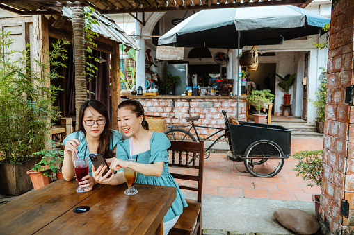 Happy women sitting and enjoying beverages in an outdoor cafe setting in Hanoi, Vietnam, sharing a moment, using a mobile phone