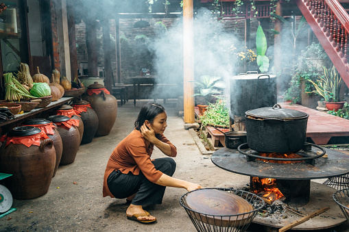 A vibrant outdoor cooking scene with large pots over open flames, surrounded by greenery near Hanoi, Vietnam.