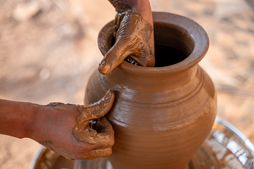 Potter making pot by giving shape to it by using fingers from both the inside and outside to mud.