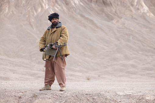 Taliban soldier with machine gun on a desert mountain in afghanistan