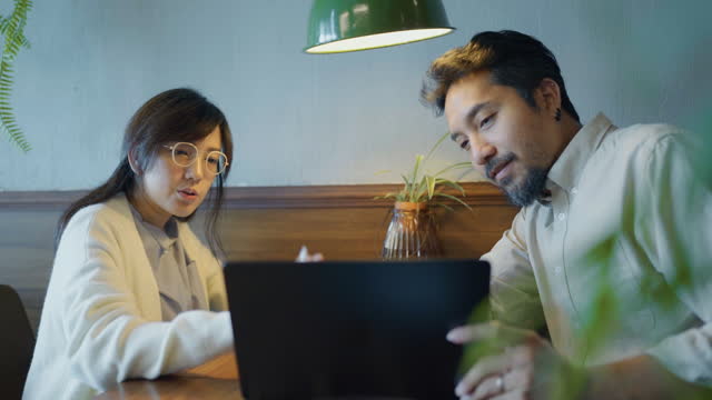 Handsome male employee is working with a laptop and a female colleague is using a digital tablet for the work they are doing together at a restaurant.