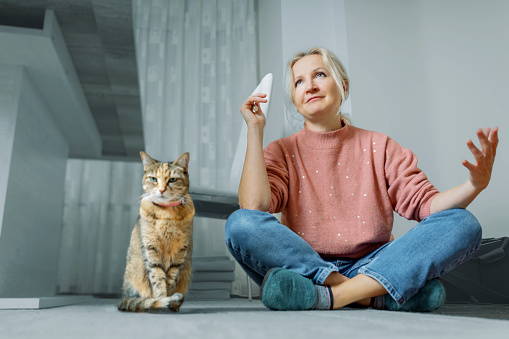 A woman talks to a cat while sitting on the floor at home