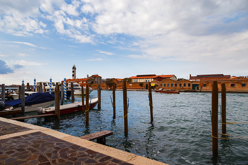 Murano, Italy - October, 6 2019: Typical street on Murano island in Venice, wharf for gondolas and boats, glass blowing factories and Murano Lighthouse or Faro di Murano.