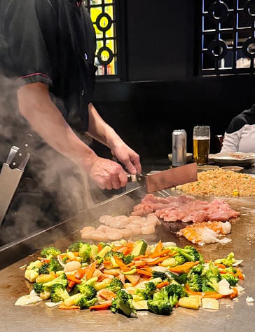Teppanyaki Chef preparing vegetables, fried rice and seafood on a Teppan in a Japanese Restaurant