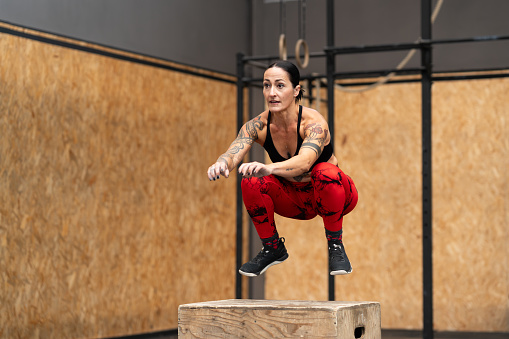 Motion photo of a strong sportive woman jumping into box in a gym