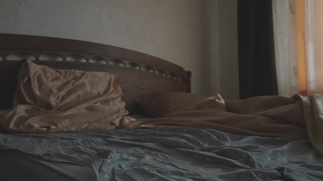 Bed with brown sheets and pillows in dimly lit room with muted colors and cinematic feel
