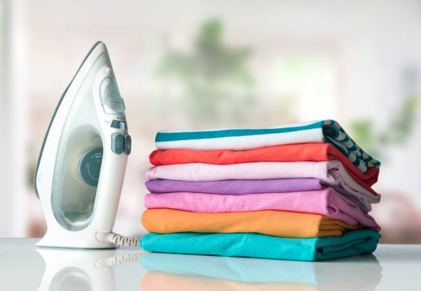 Colorful cotton shirts folded stack on table with iron. Household concept. Spring summer clothes.Washed linen.