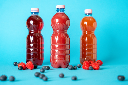 Three bottles of berry-flavored juice surrounded by fresh raspberries and blueberries on a vibrant blue backdrop.