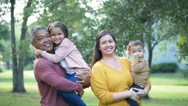 Multiracial parents lift up children, smile at camera