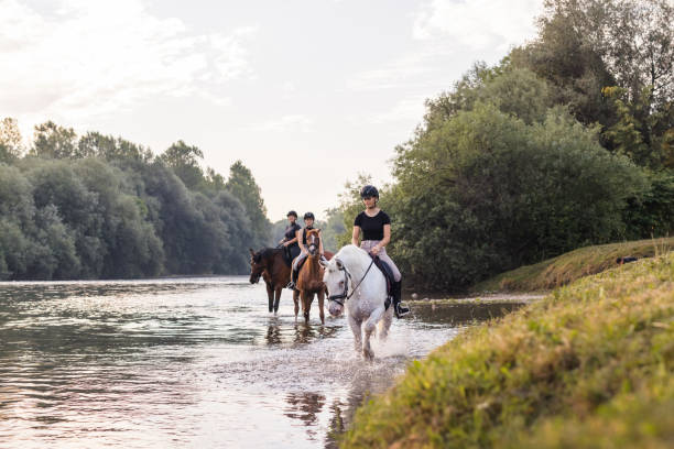 istock Three girls horseback riding across the river during sunset 2092171088