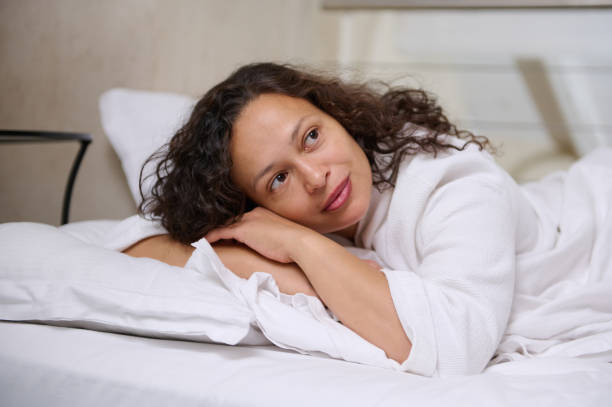 istock Beautiful young woman dreamily looking away, falling asleep on white soft bed sheets on her comfortable bed in bedroom 2092228049