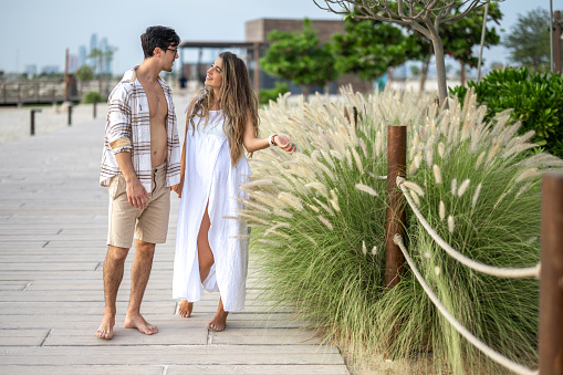 Beautiful young pregnant woman holding hands with her husband and having conversation about their future life with expected child outdoors.