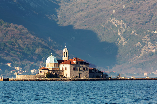 Our Lady of the Rocks Church stands on an islet in Kotor Bay, with a mountainous backdrop. Perast, Montenegro