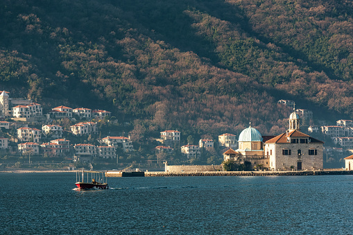 Tourist boat sails from the Orthodox Church of Our Lady of the Rocks in Kotor Bay, with a mountainous backdrop. Perast, Montenegro