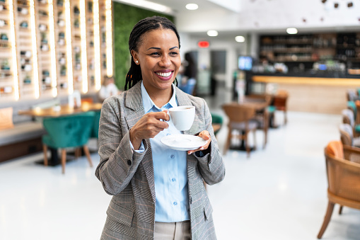 Portrait of happy African businesswoman holding cup of coffee at coffee shop