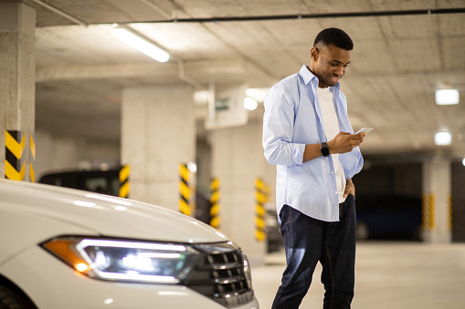 Black man looking at the phone at his car in the parking lot. High quality photo