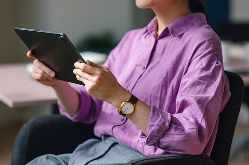 Cropped shot of a woman in a purple blouse using a digital tablet.
