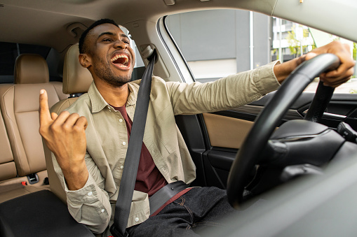 Joyful black man dancing in car, singing while driving his car. Road fun. High quality photo