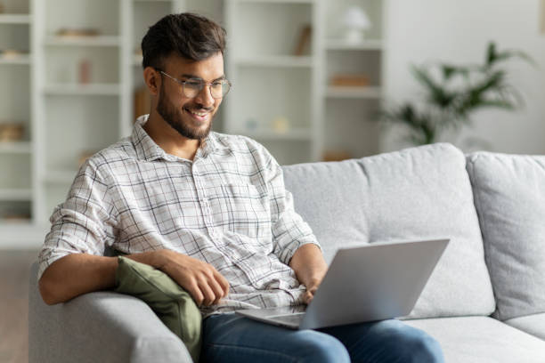istock Positive hindu man freelancer working using laptop computer sitting on couch at home interior, guy surfing Internet, using modern technologies, free space 2092363709