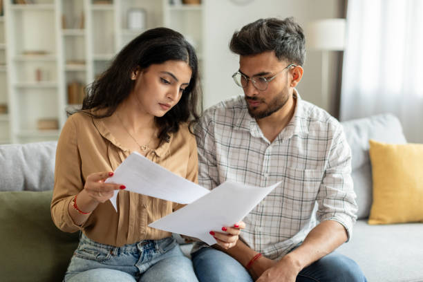 istock Indian couple checking bills, reading documents, unhappy man and woman holding papers, counting monthly spendings, sitting on sofa at home 2092374676
