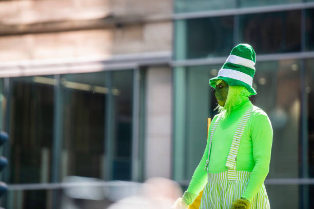 A stereotypical Irish character all ready for Saint Patricks day.  He gives two thumbs up, a big smile on his face.  Studio portrait.  Horizontal image with copy space.  Green striped wallpaper background.