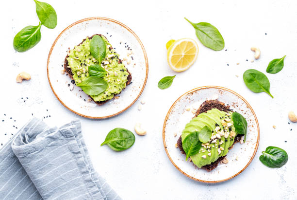 toasts à l’avocat avec épinards et noix de cajou saupoudrés de graines de sésame sur fond de table blanc, vue de dessus - appetizer bread breakfast cashew photos et images de collection