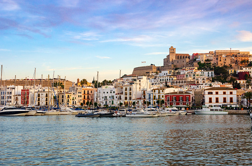 An image capturing the historic beauty of Ibiza Old Town, Dalt Vila, bathed in the warm glow of sunset. The ancient walls and charming architecture of this UNESCO World Heritage site are highlighted against the backdrop of the setting sun, showcasing the timeless elegance and Mediterranean charm of this iconic destination.