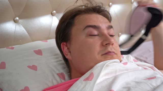 Young man wakes up on bed with sheets decorated with hearts