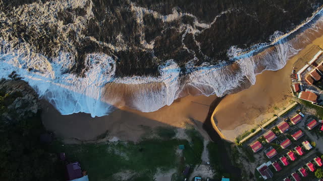 Aerial view down to a sandy beach being hit by storm waves