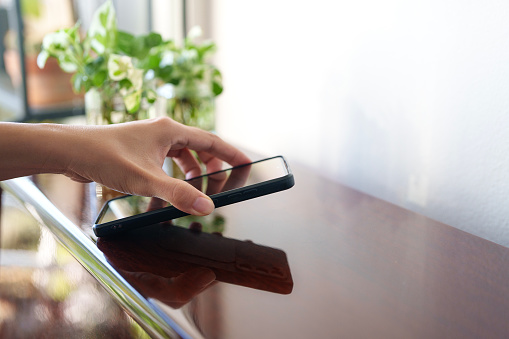 Cropped shot of a hand grabbing and picking up a mobile phone from the table.