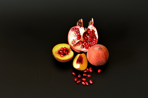 Pieces of a ripe peach and a broken pomegranate fruit with seeds on a black background. Close-up.