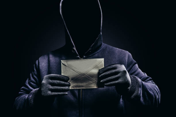 Photo of scary hooded man holding letter. Photo of scary shaded hooded man holding paper letter on dark background. suspicious message stock pictures, royalty-free photos & images