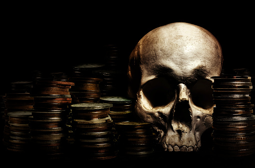 Photo of shaded human skull laying amidst pile of coins.