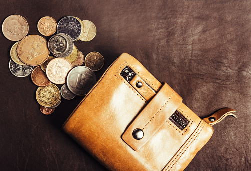 Photo of leather closed wallet laying on leather table with various coins.